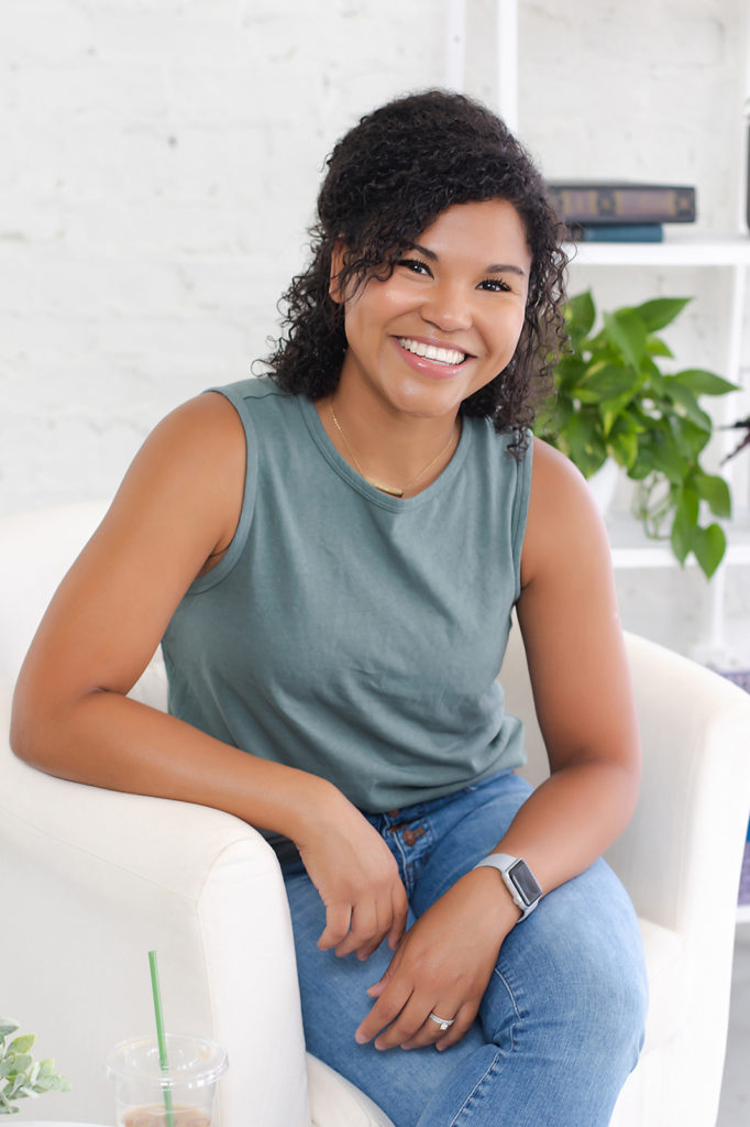 Picture of smiling biracial woman sitting down on a white accent chair