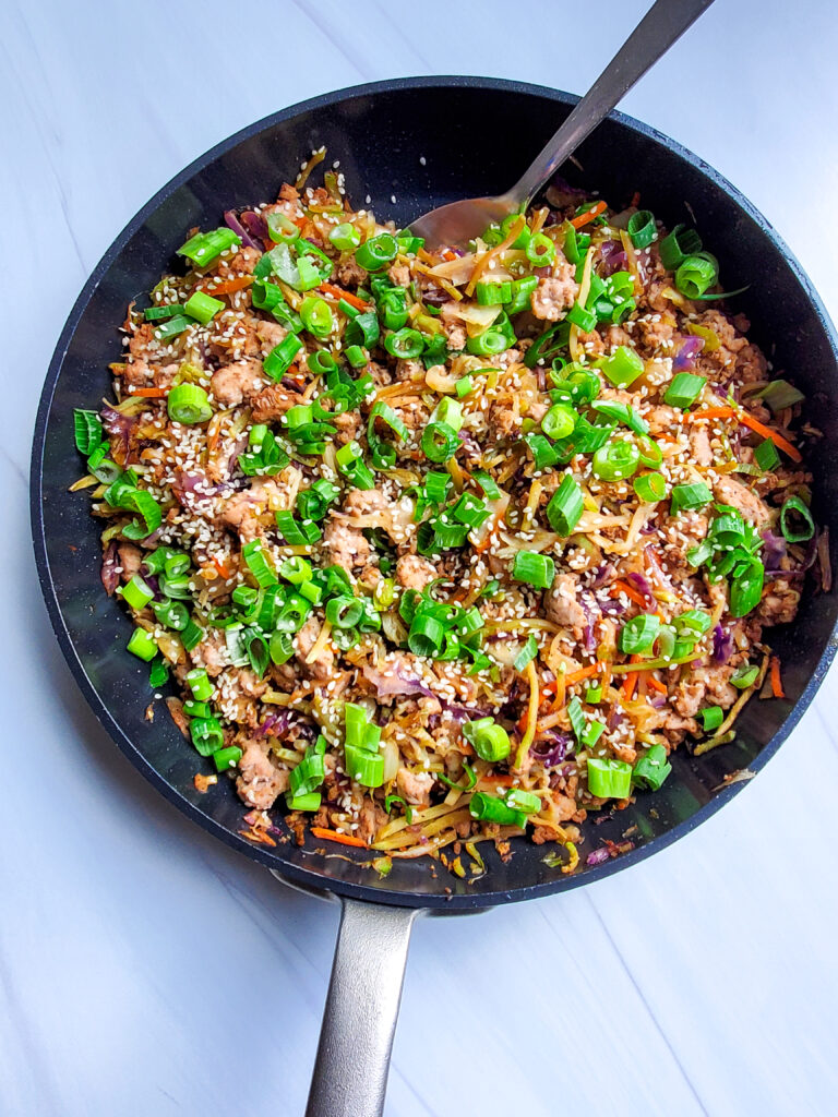 Egg Roll in a Bowl with ground turkey, cabbage, carrots, and green onions served in a black skillet on a white table.