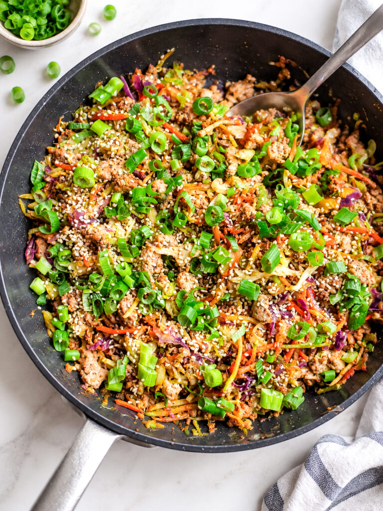 Easy Egg Roll in a Bowl with ground pork, cabbage, carrots, green onions, and sesame seeds in a skillet.