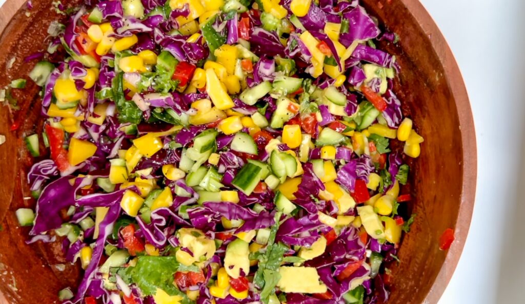 Bright and colorful Rainbow Mango Chopped Salad with red cabbage, mango, avocado, corn, and lemon maple dressing in a white serving bowl.
