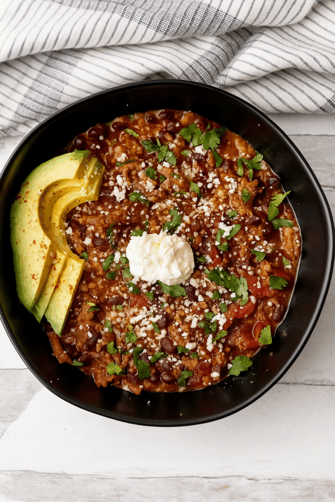 Bowl of veggie-packed turkey chili topped with avocado, sour cream and cilantro