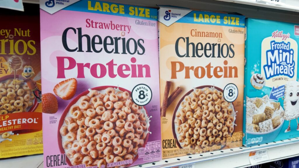 Close-up of grocery store cereal shelf featuring high-protein cereals, including multiple boxes labeled “protein,” highlighting the trend of protein-enriched foods.
